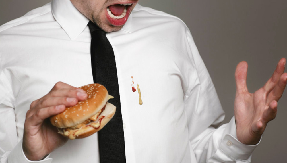 Un hombre se mancha la camisa comiendo una hamburguesa