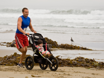 Un hombre corre en la playa con un bebé Un hombre corre en la playa con un bebé