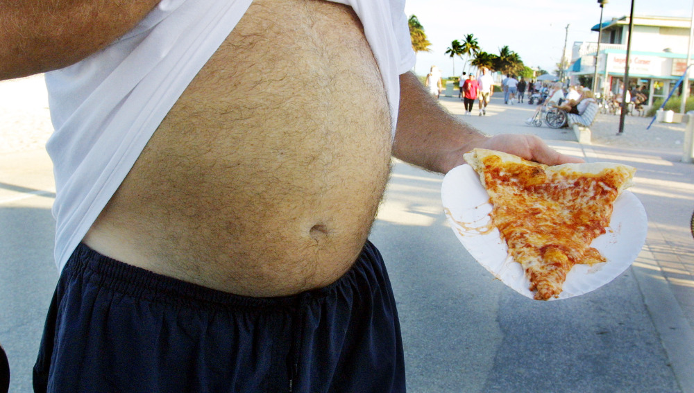 Un hombre come una pizza en el paseo marítimo