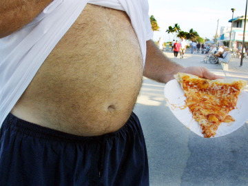 Un hombre come una pizza en el paseo marítimo